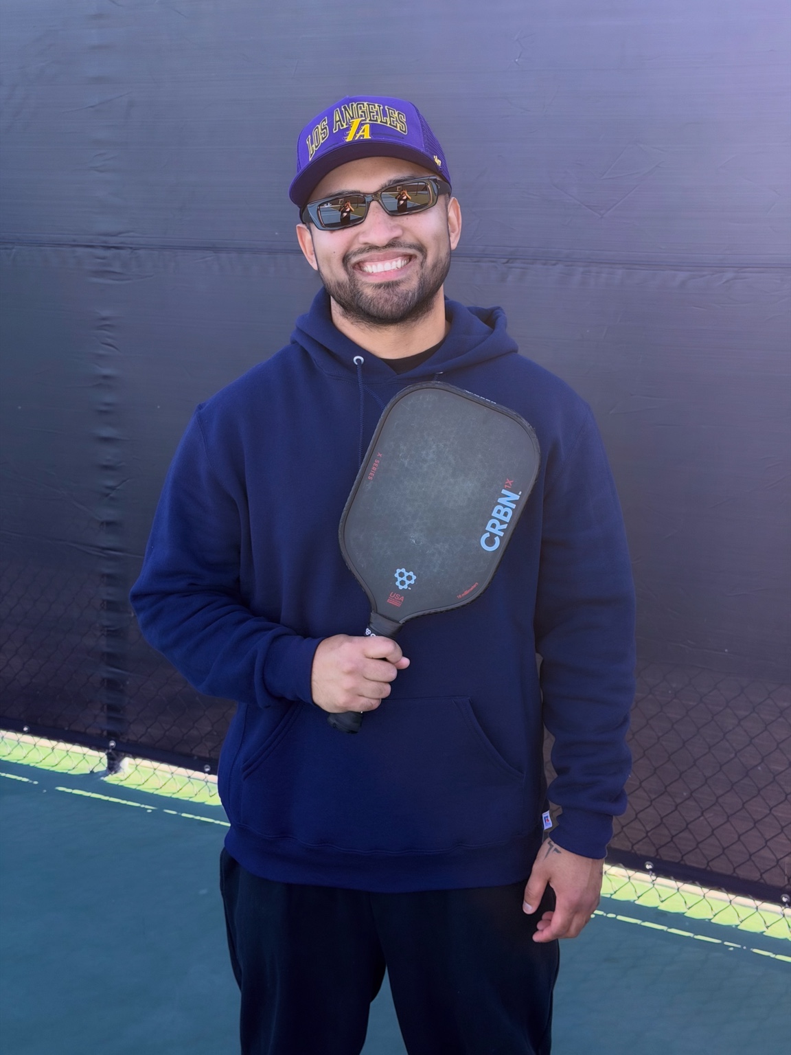 Sean holding his paddle, wearing a purple Los Angeles cap and navy hoodie